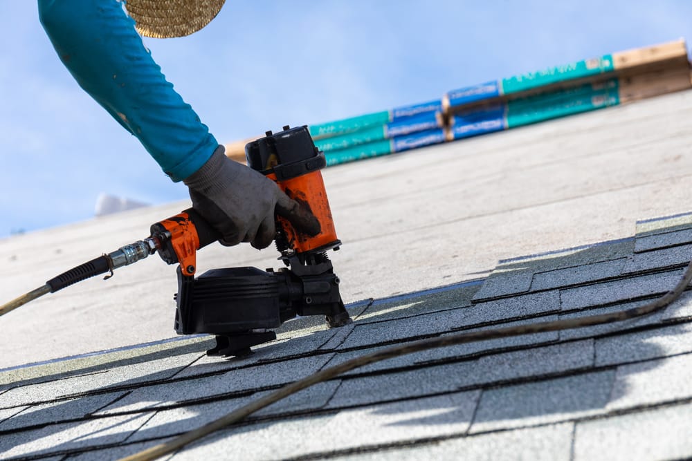 A man is installing shingles on a roof with a nail gun